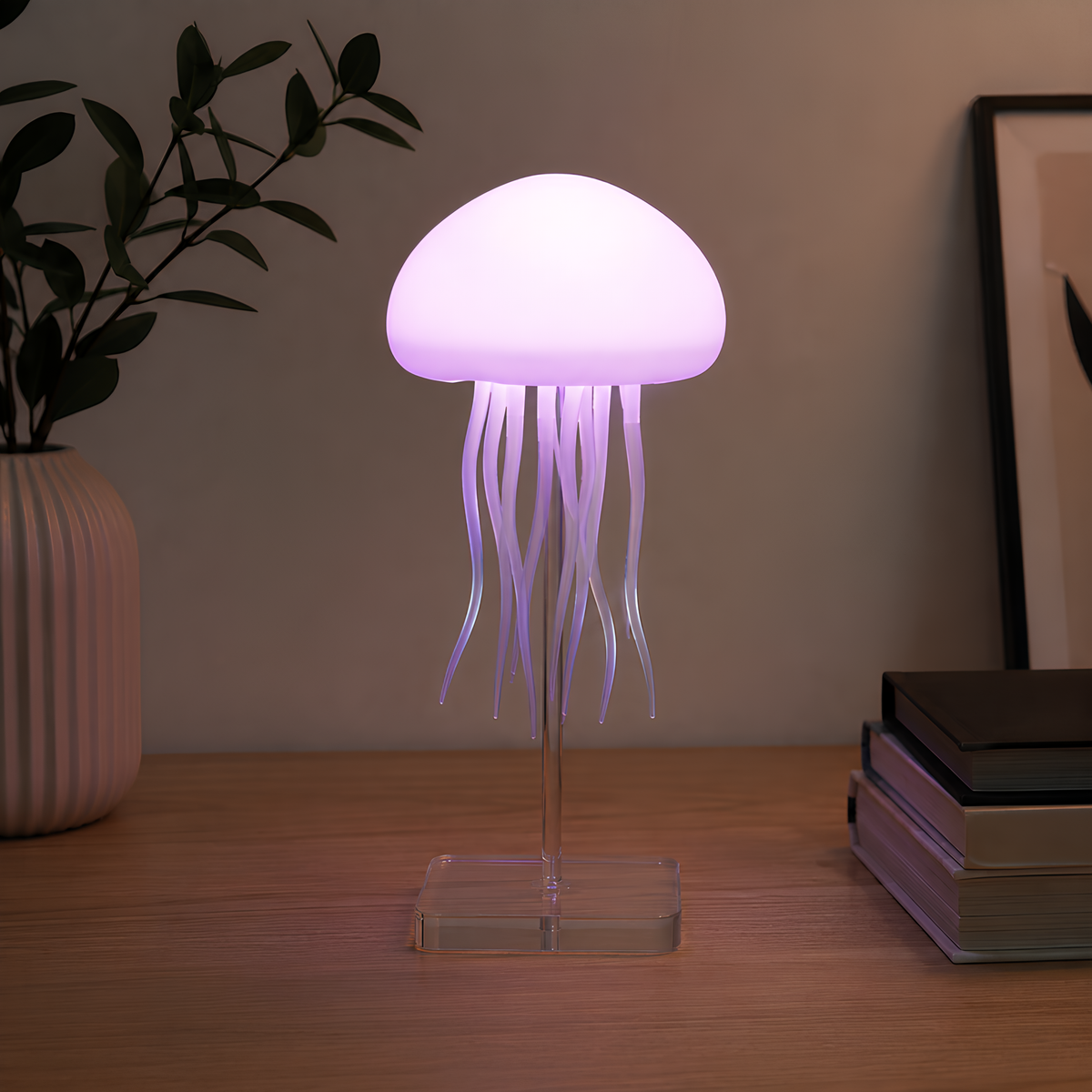 A jellyfish-shaped table lamp with a glowing purple-white dome and translucent tentacles on a clear acrylic stand, placed on a wooden tabletop with a vase and books in the background.